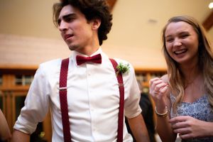 A young man in suspenders and bow tie mingles with guests at a wedding reception.