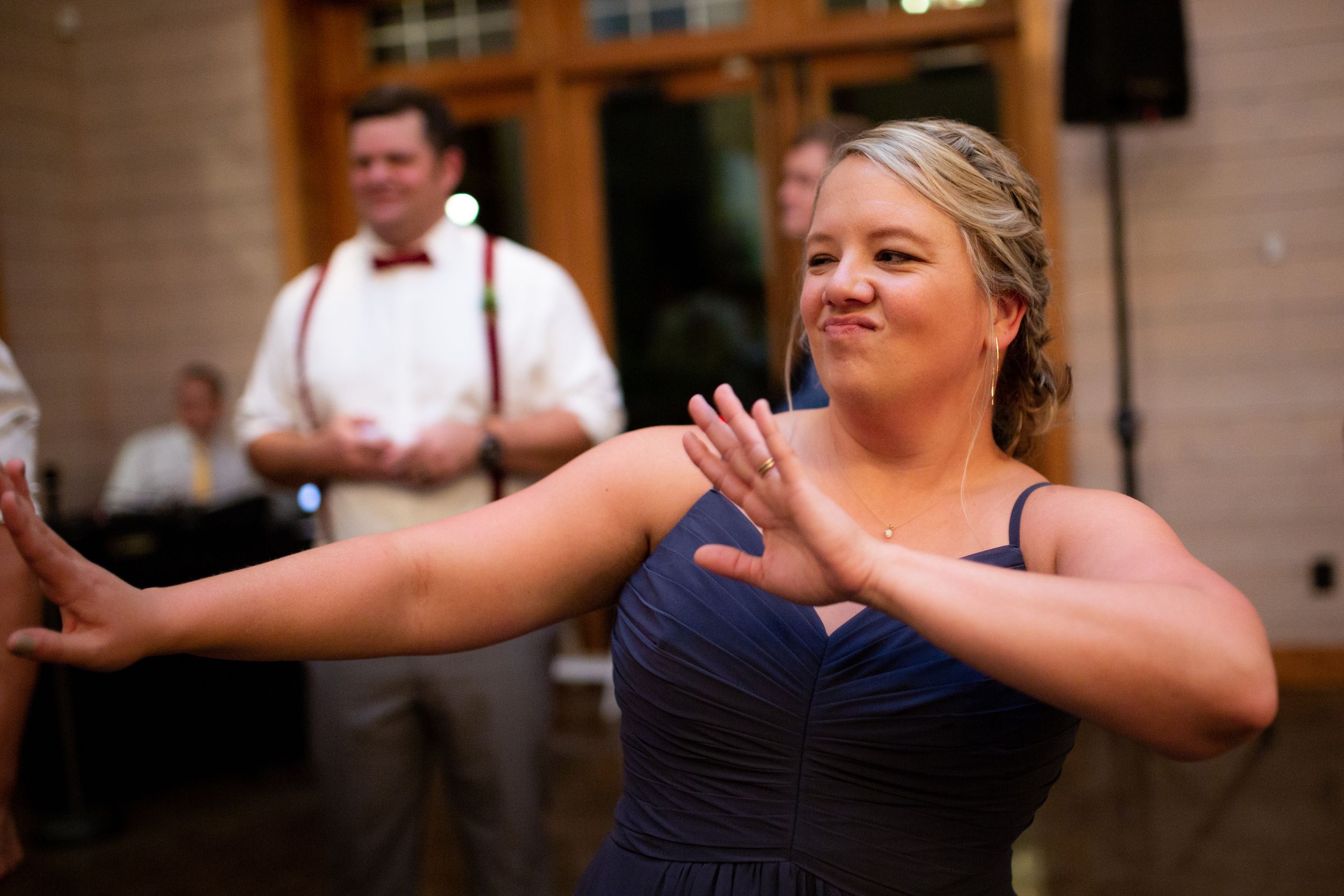A bridesmaid in a navy dress dances enthusiastically at the reception.