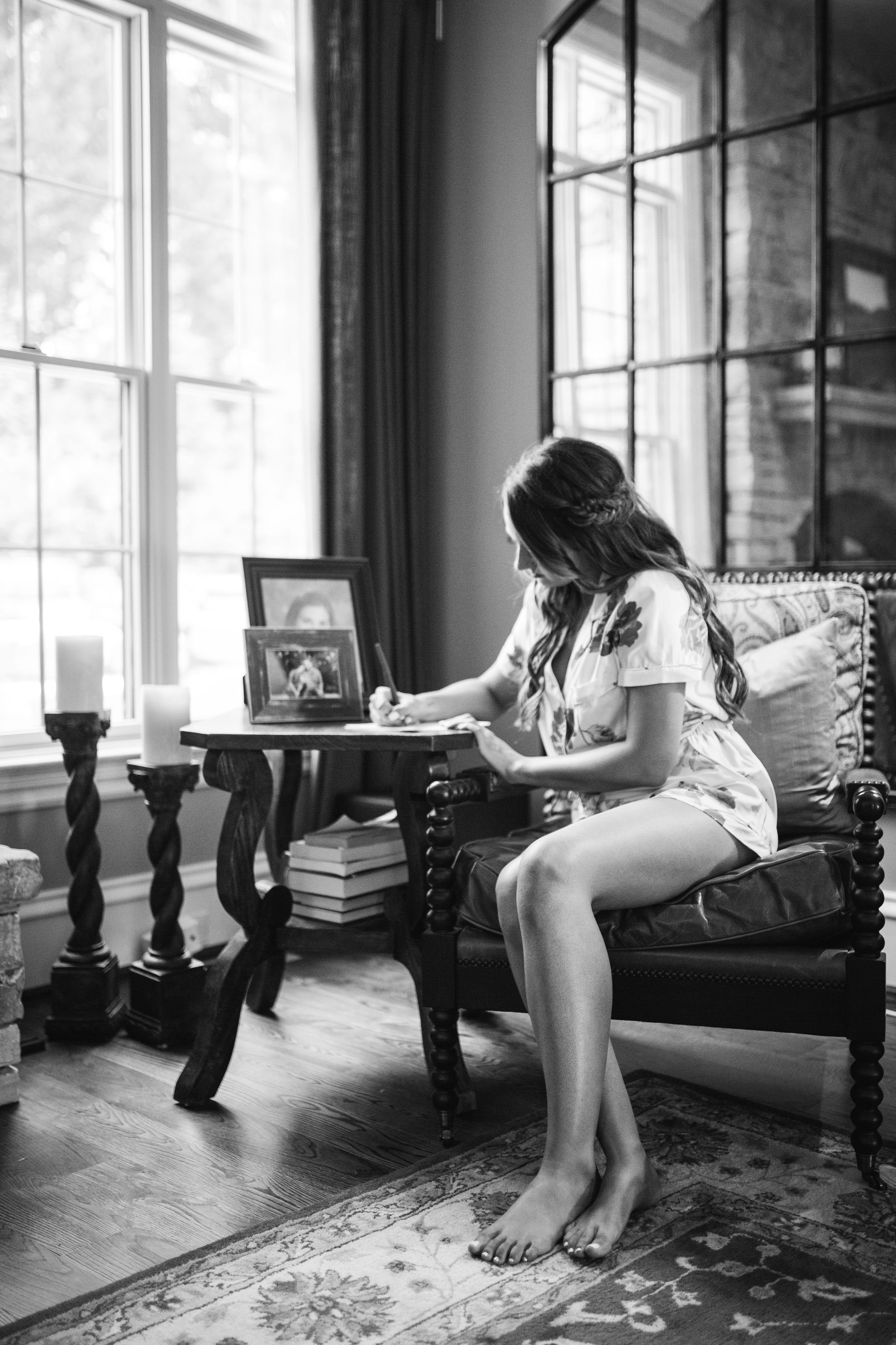 A contemplative moment captured in black and white by a window with candlesticks and vintage furniture.