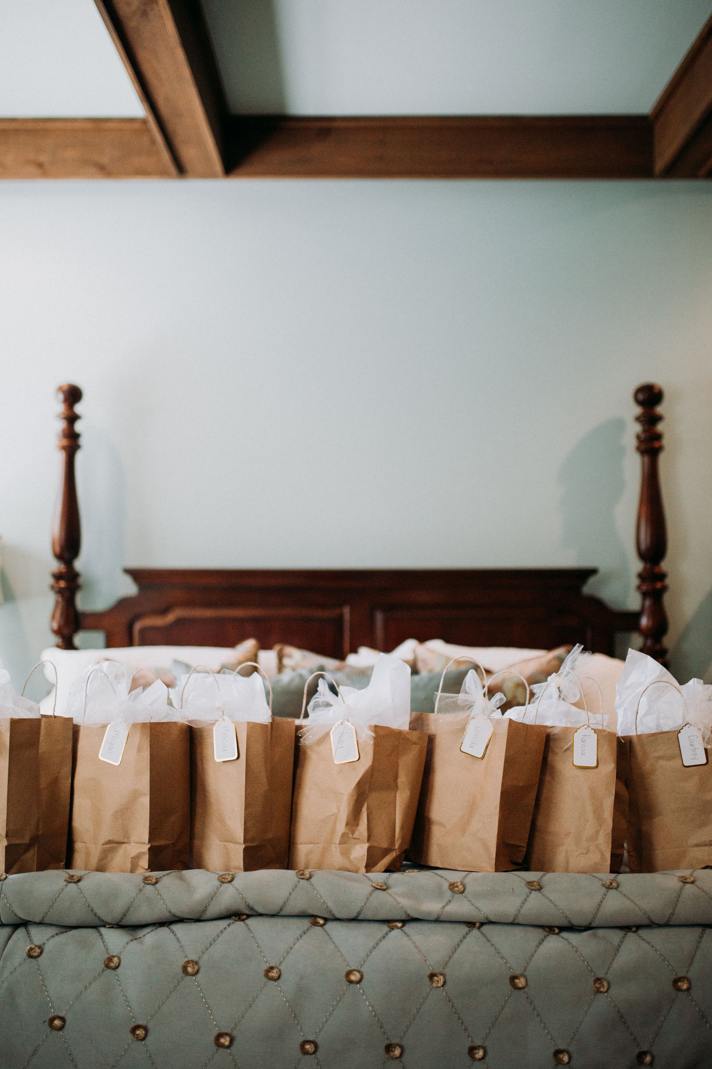 Row of brown paper gift bags arranged on a tufted grey bench against a white wall.