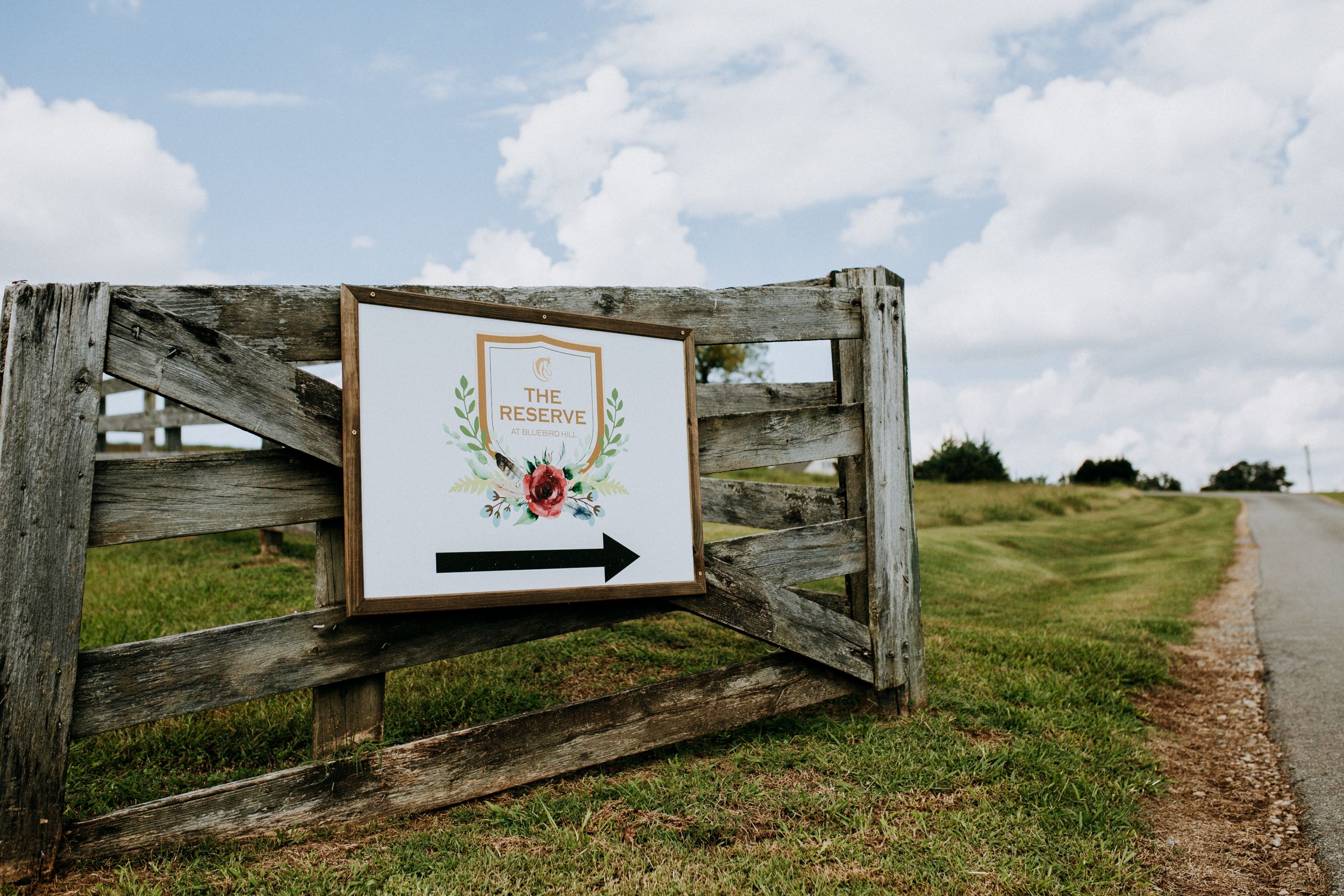 Rustic wooden gate with wedding directional sign in countryside setting.