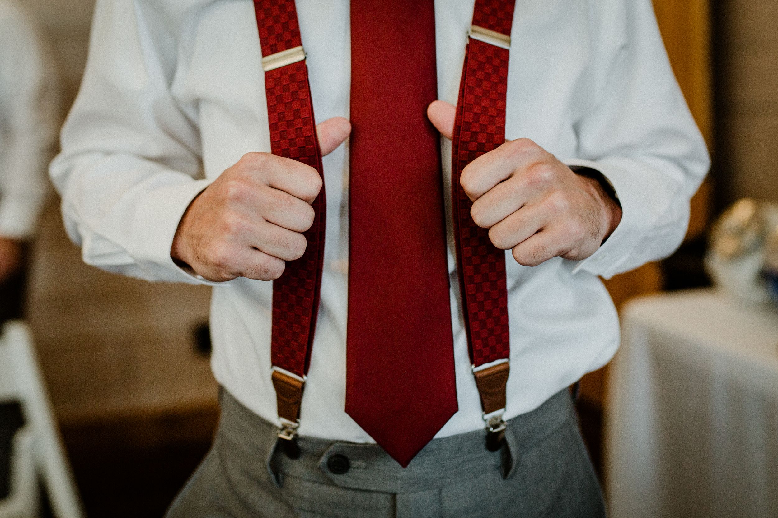 Close-up of red suspenders and tie worn with white shirt and grey pants.
