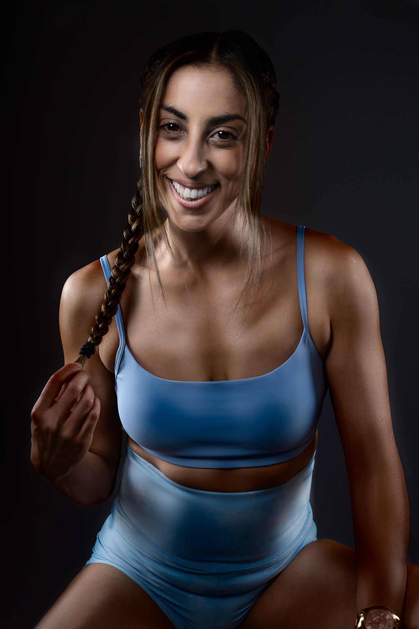 Athletic portrait in light blue workout set with braided hair and joyful expression.