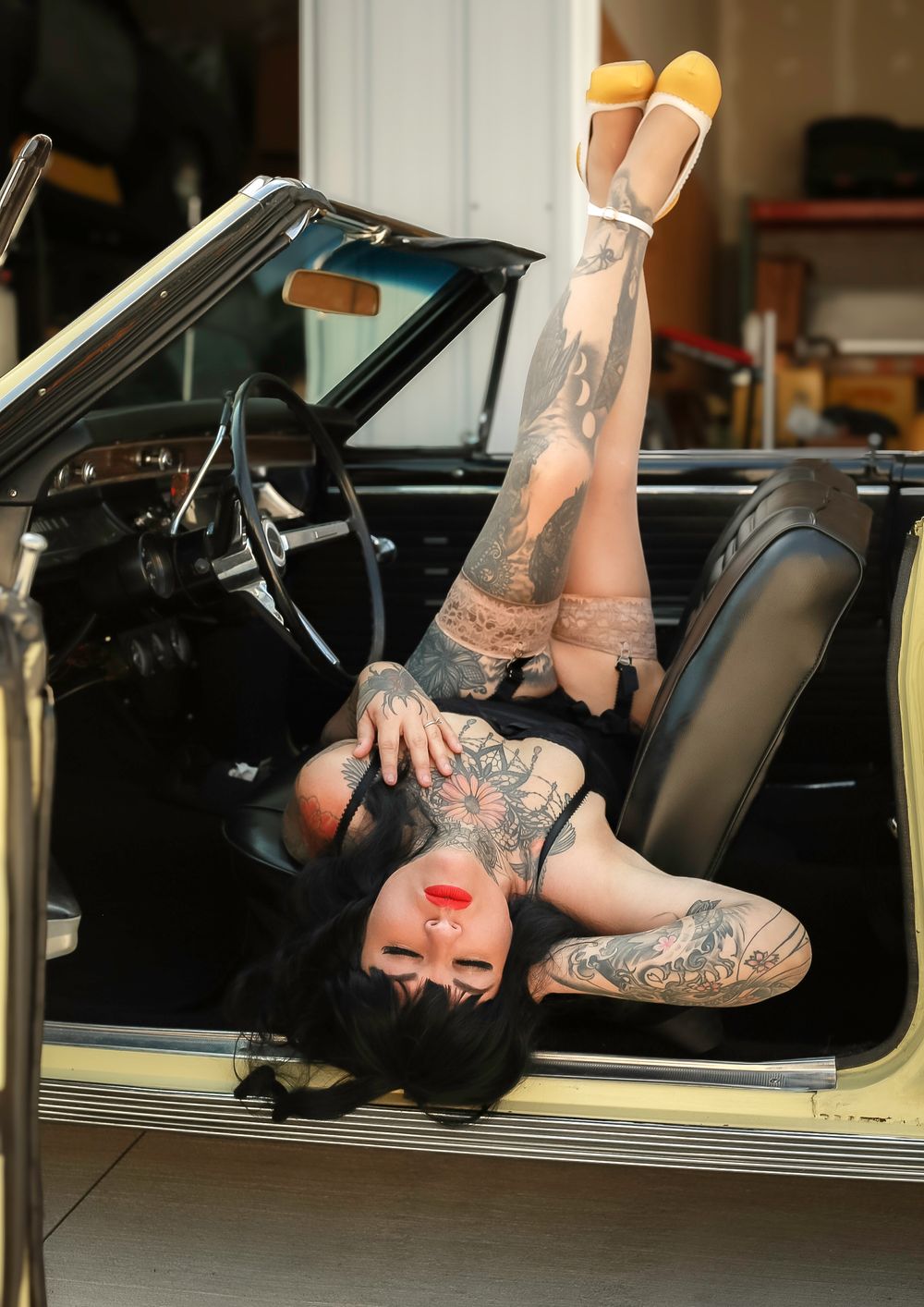Classic vintage convertible car interior featuring yellow heels and lace stockings with ornate tattoo designs.
