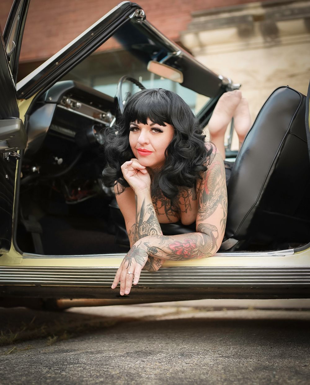 Vintage car with retro styled model showing tattoos and black hair leaning out the passenger side door.
