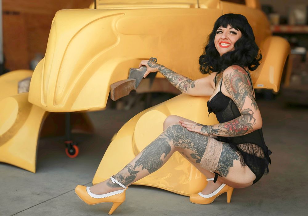 Tattooed model in black lingerie posing playfully on bright yellow custom car.