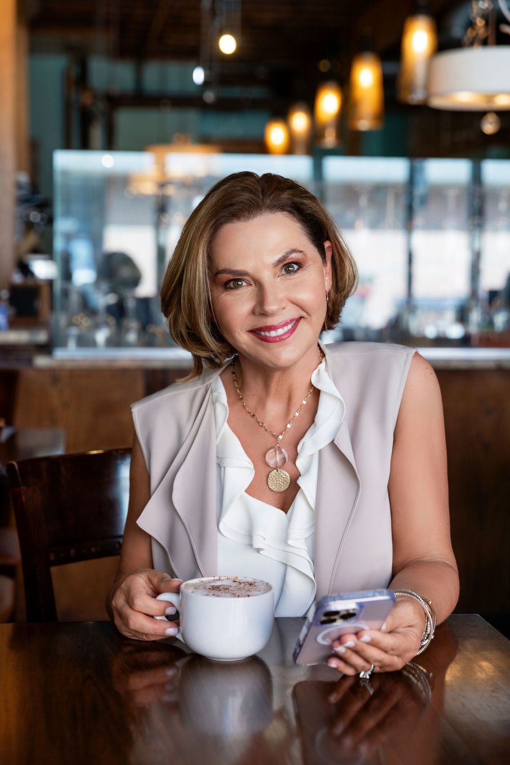 A person in a white ruffled blouse enjoys coffee at a restaurant with warm ambient lighting.