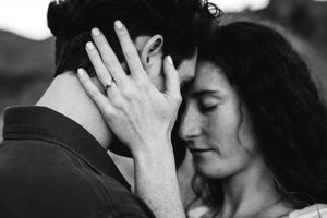 Black and white close-up of couple nearly kissing with engagement ring visible.