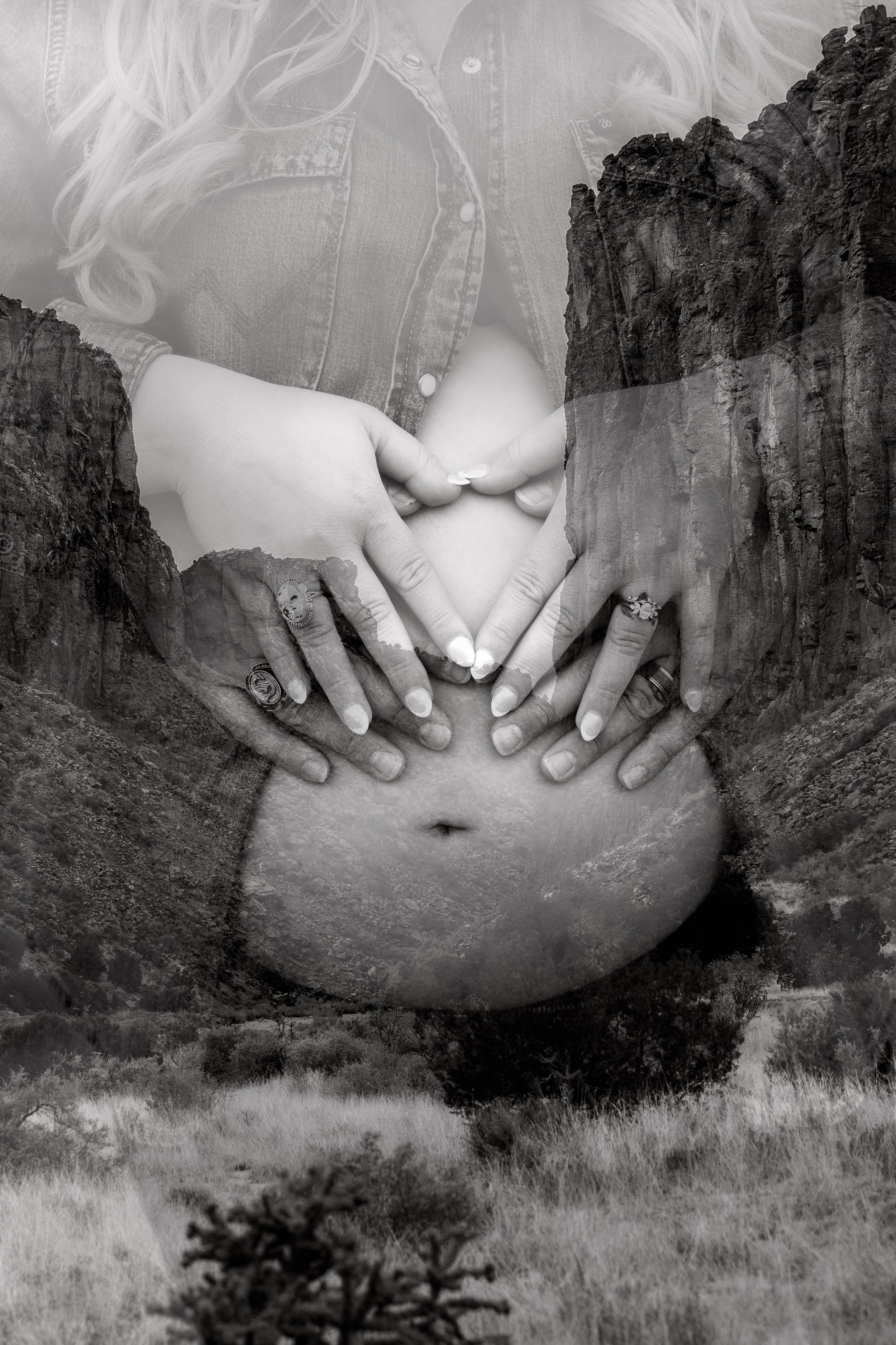Black and white double exposure maternity photo with couple forming heart shape on pregnant belly against rocky landscape.