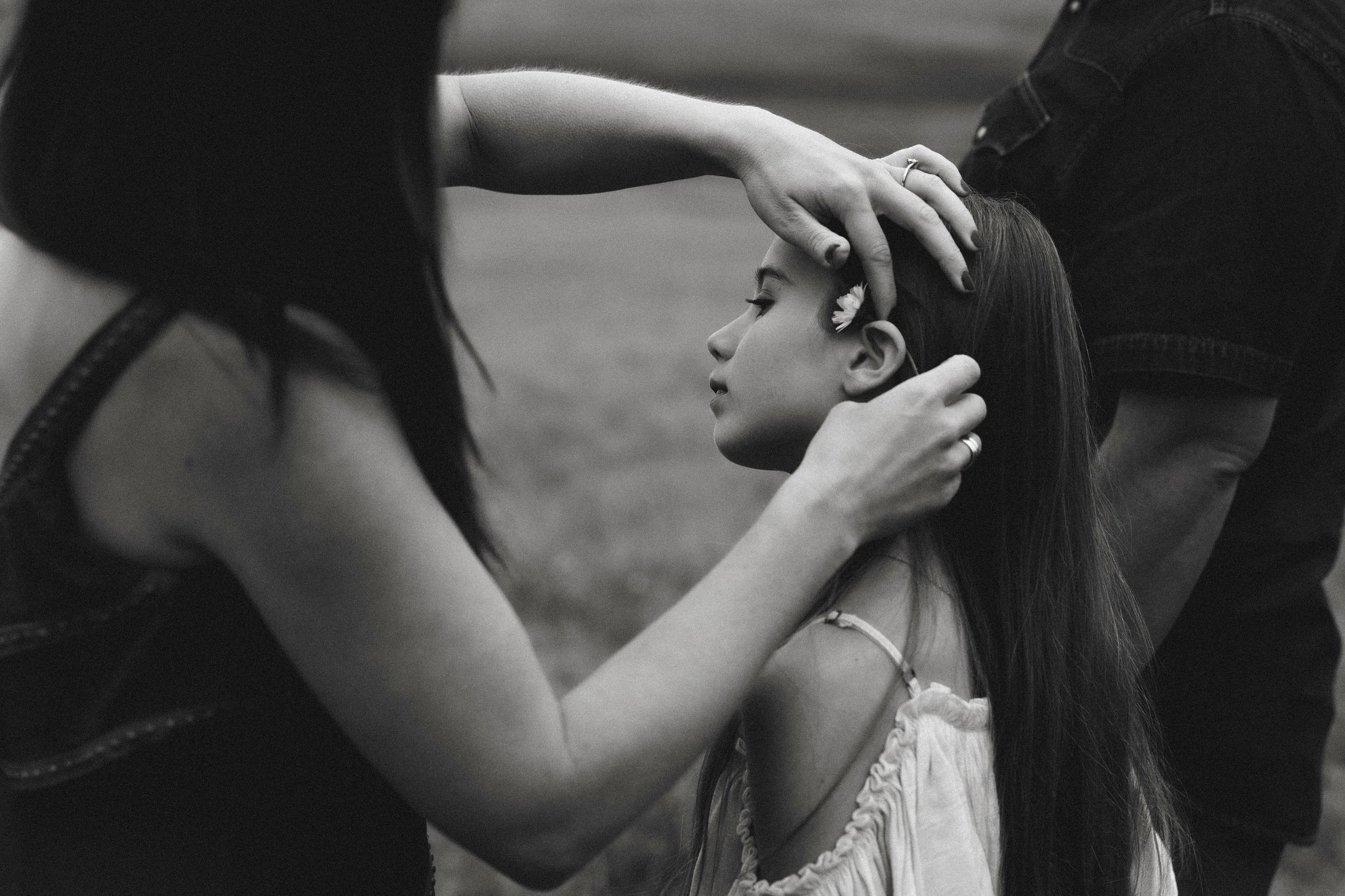 Black and white photo of parents gently touching their young daughters long hair outdoors.