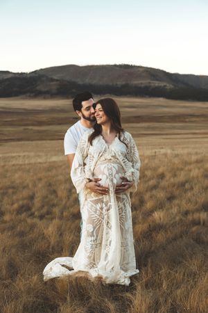 Couple sharing intimate moment in golden Valle Grande, woman in lace maternity gown.