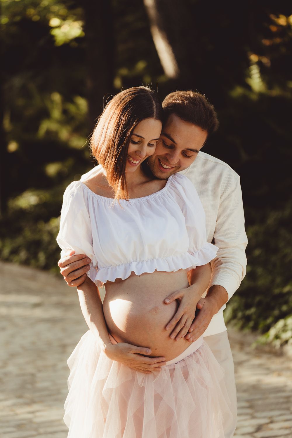Romantic maternity photo session showing couple embracing in soft natural light outdoors.
