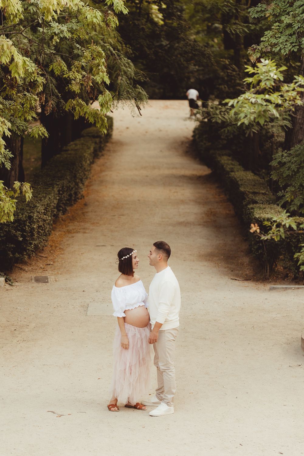 A couple walks together on a winding garden path surrounded by lush green foliage on a sunny day.