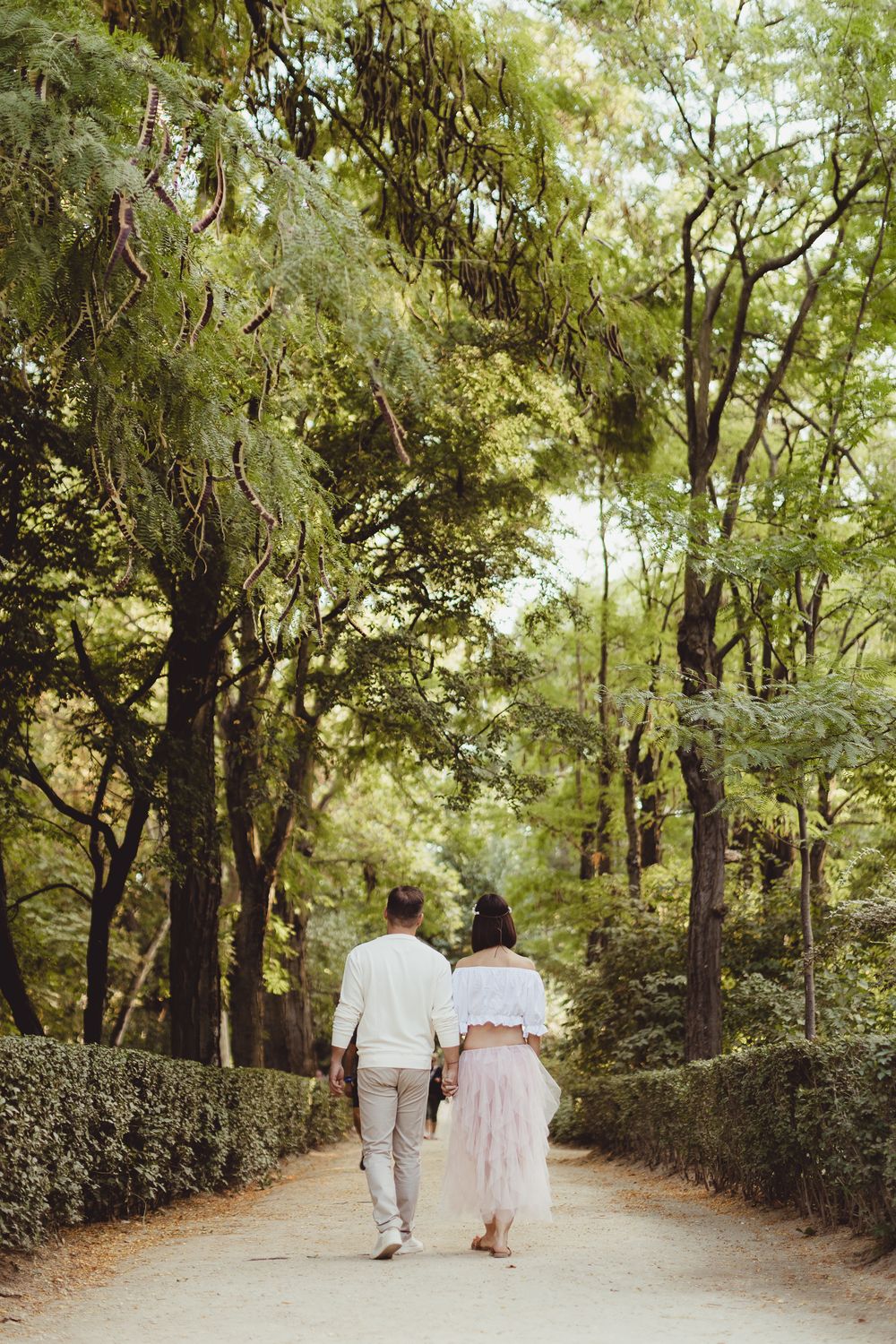 Two people walk together on a peaceful tree-lined path through a lush green forest.