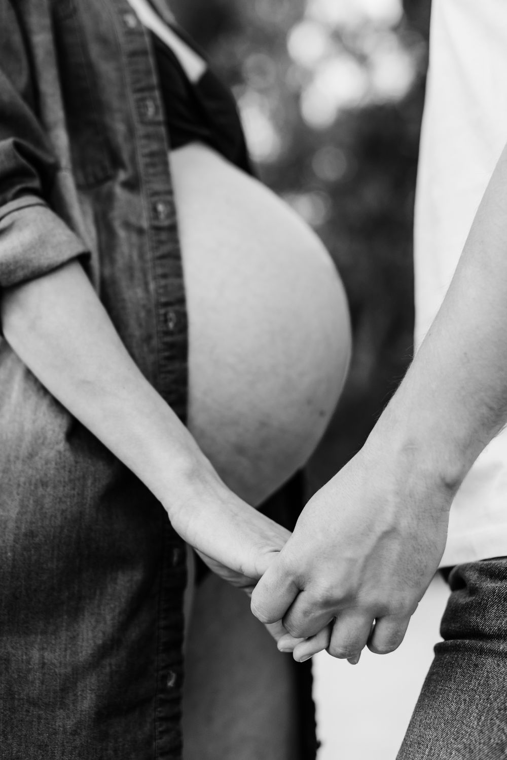 A black and white close-up photograph shows two people holding hands together in a tender moment.
