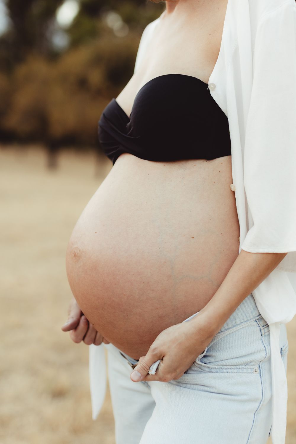 Side view progression photos showing a growing pregnant belly against light colored clothing on a beach background.