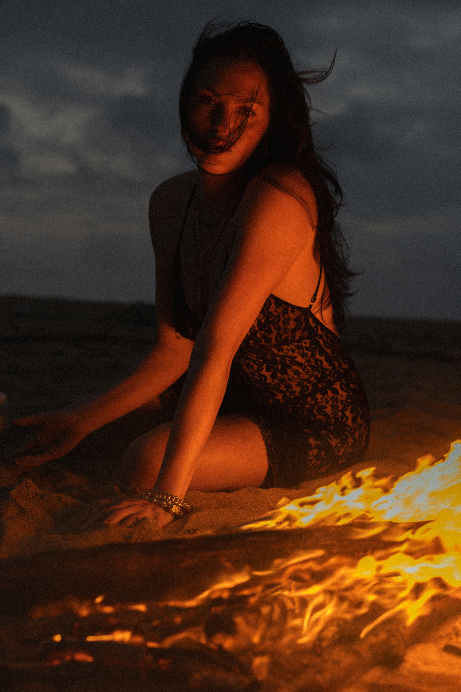 Fire illuminates dark beach scene with dramatic orange glow against night sky.