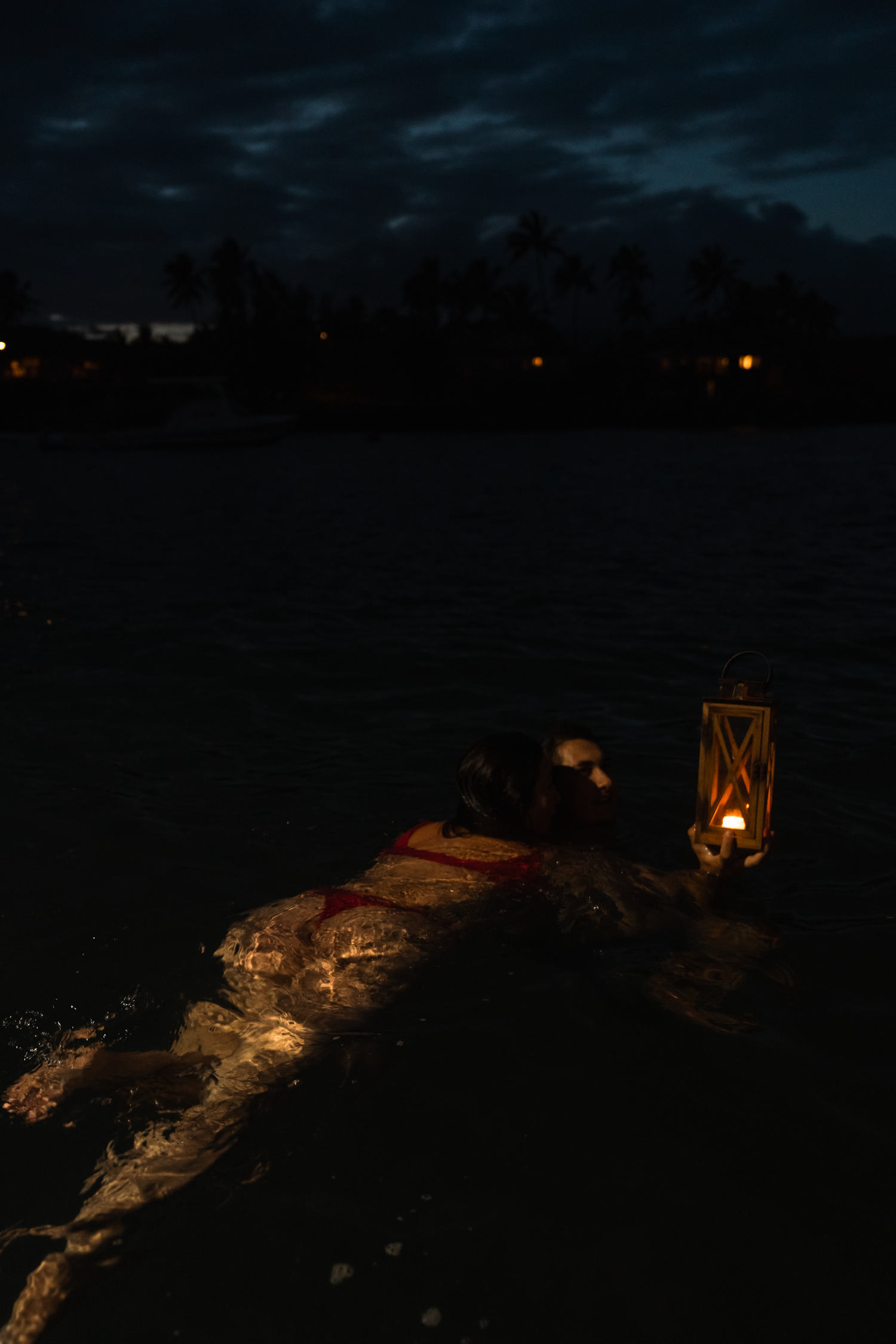 Lanterns illuminate wooden dock at night with dark water below.