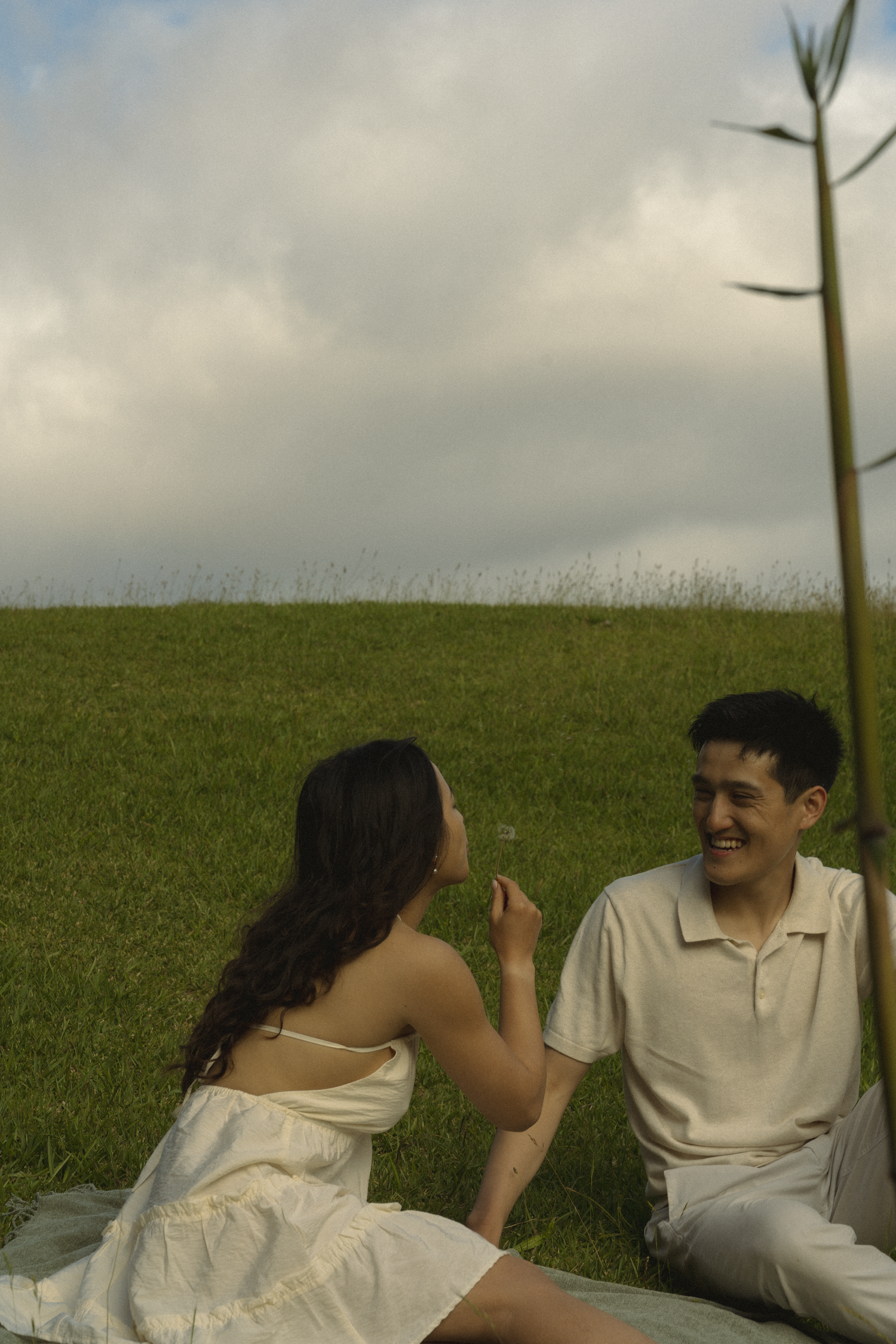 Two people sharing a lighthearted moment while sitting on grass outdoors.