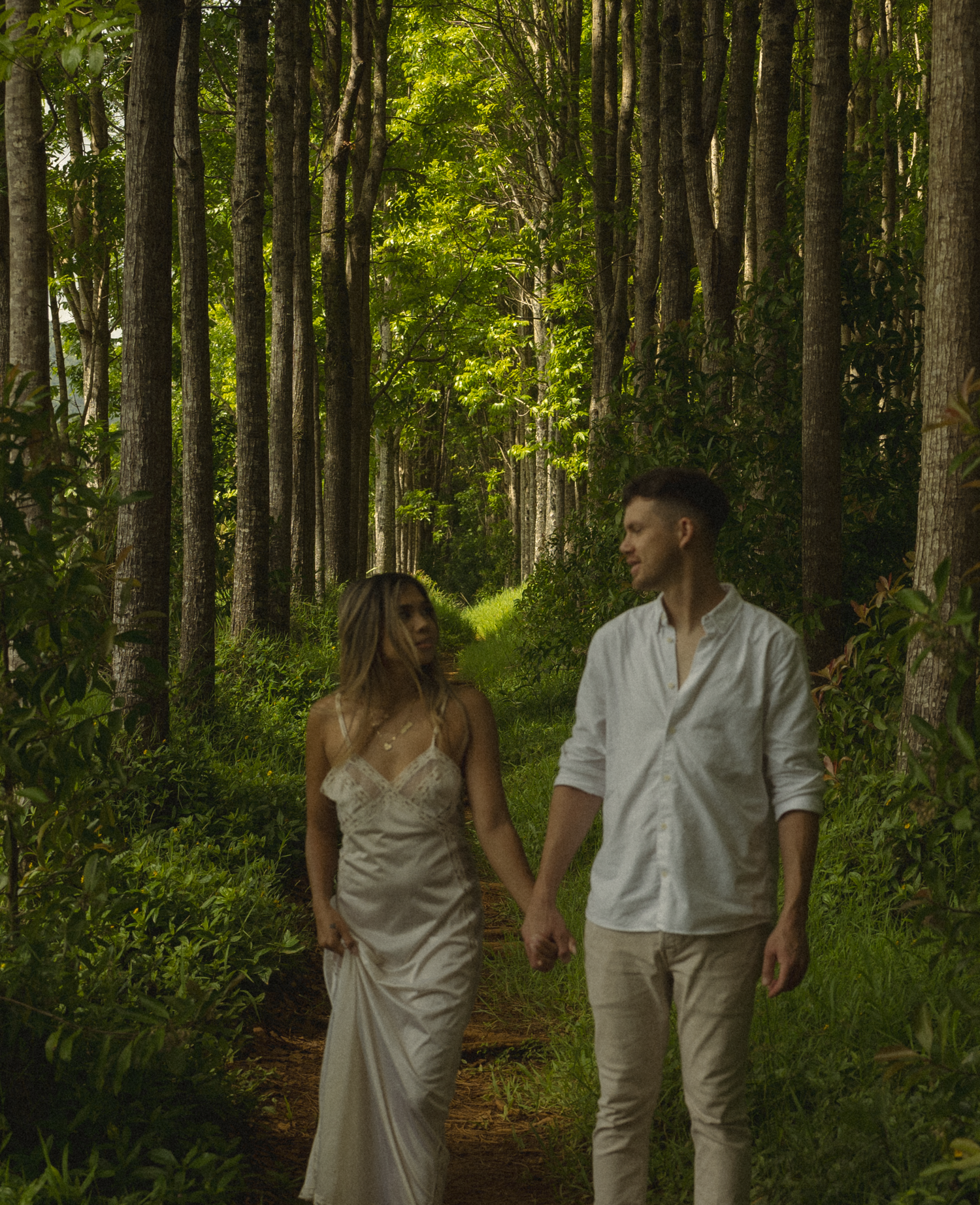 A couple walking hand in hand down a magical forest path lined with tall trees.