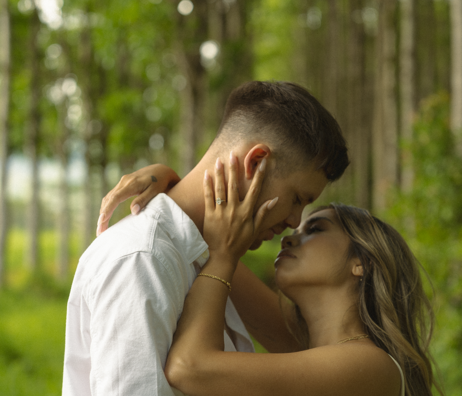 Couple enjoying an intimate moment in a lush green forest setting.