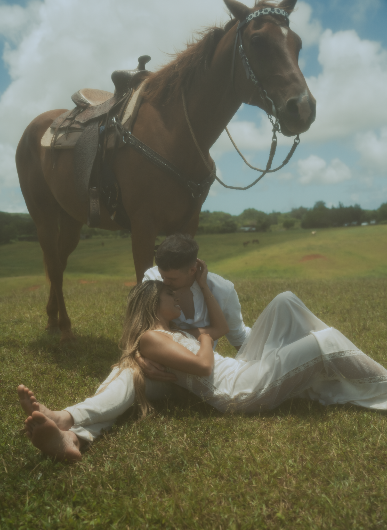 People in white clothing lying in grass next to a brown horse in a meadow.