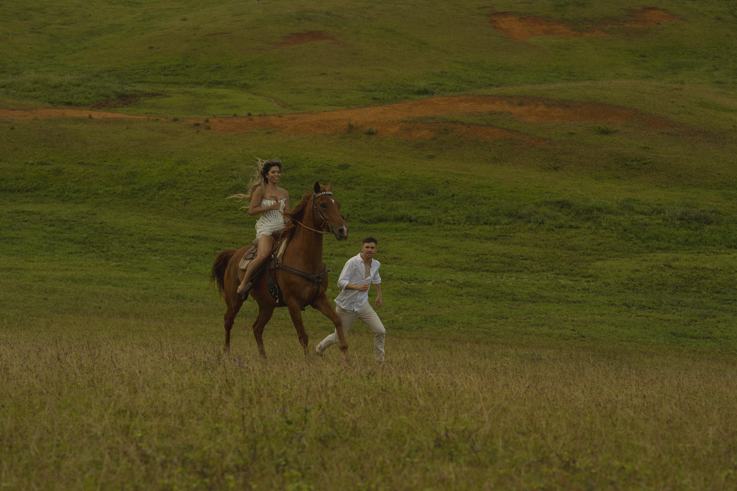 A scenic countryside image of horseback riding through a grassy field at sunset.