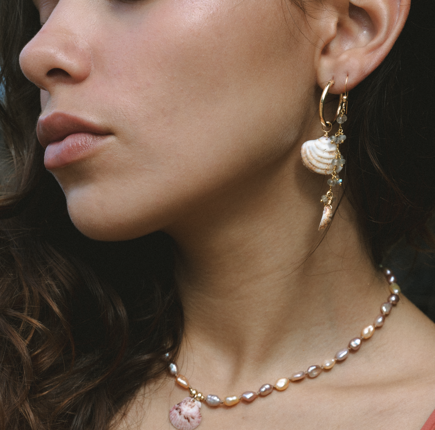 Pearl and shell drop earrings and delicate necklaces are displayed in dramatic lighting.