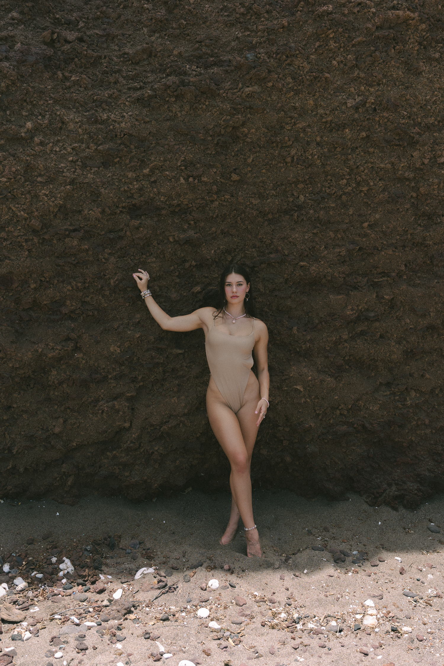 An artistic beachwear photo with someone posing against a dramatic rocky cliff wall.