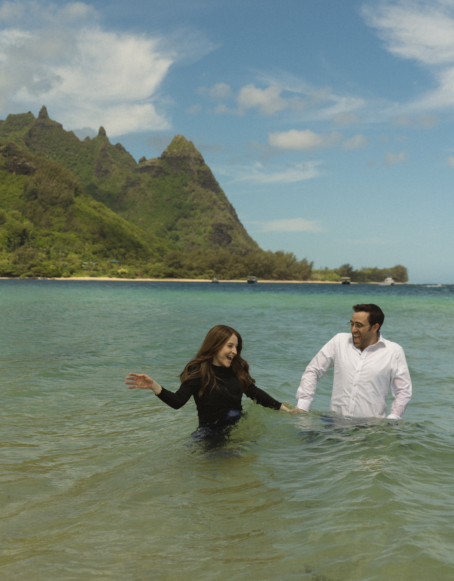 People enjoying the ocean waters near a scenic Hawaiian coastline with jagged mountains.