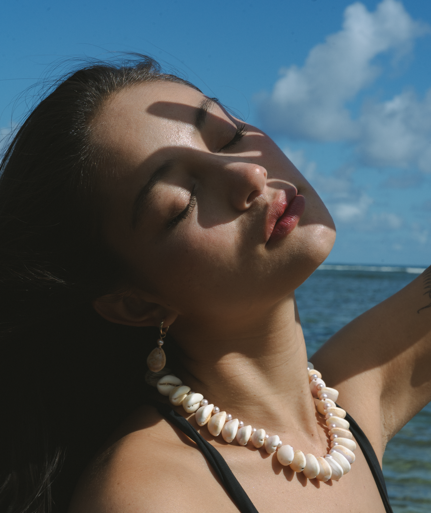 Artistic portrait with pearl necklace against ocean and blue sky backdrop.