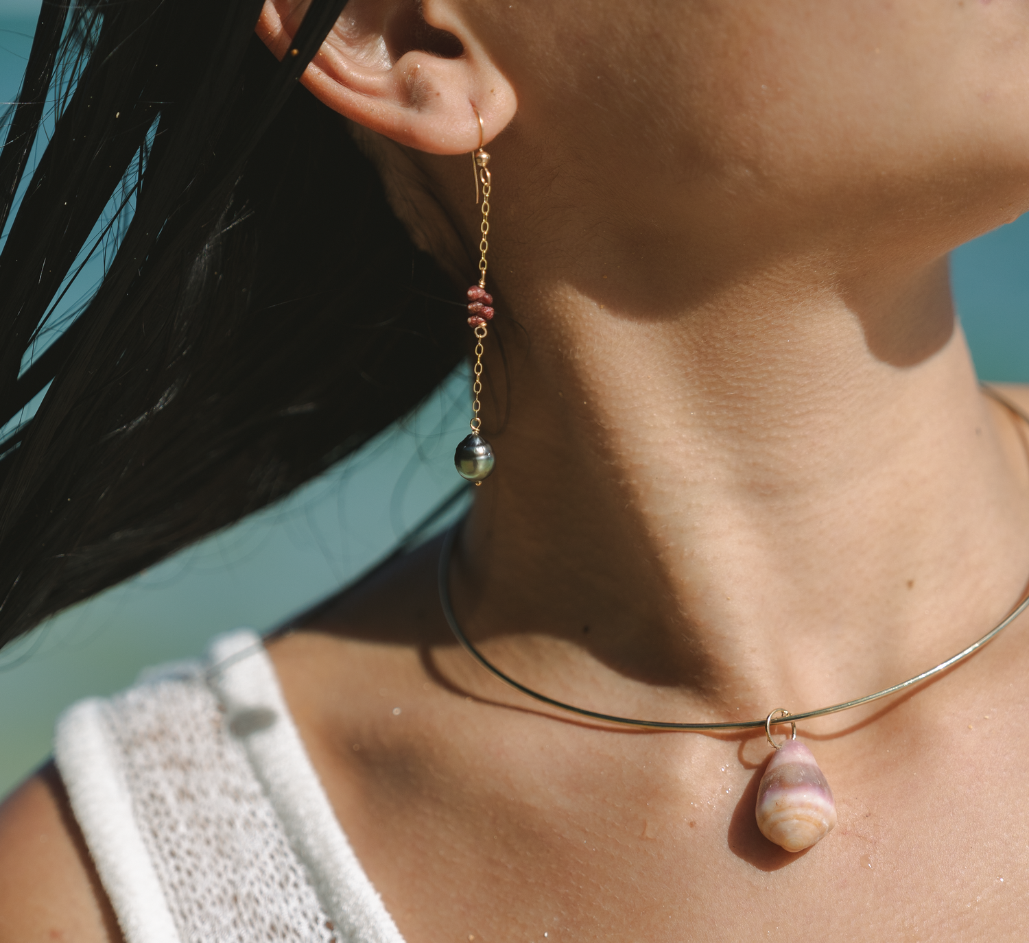 Close up detail of minimalist jewelry and neckline against beach backdrop.