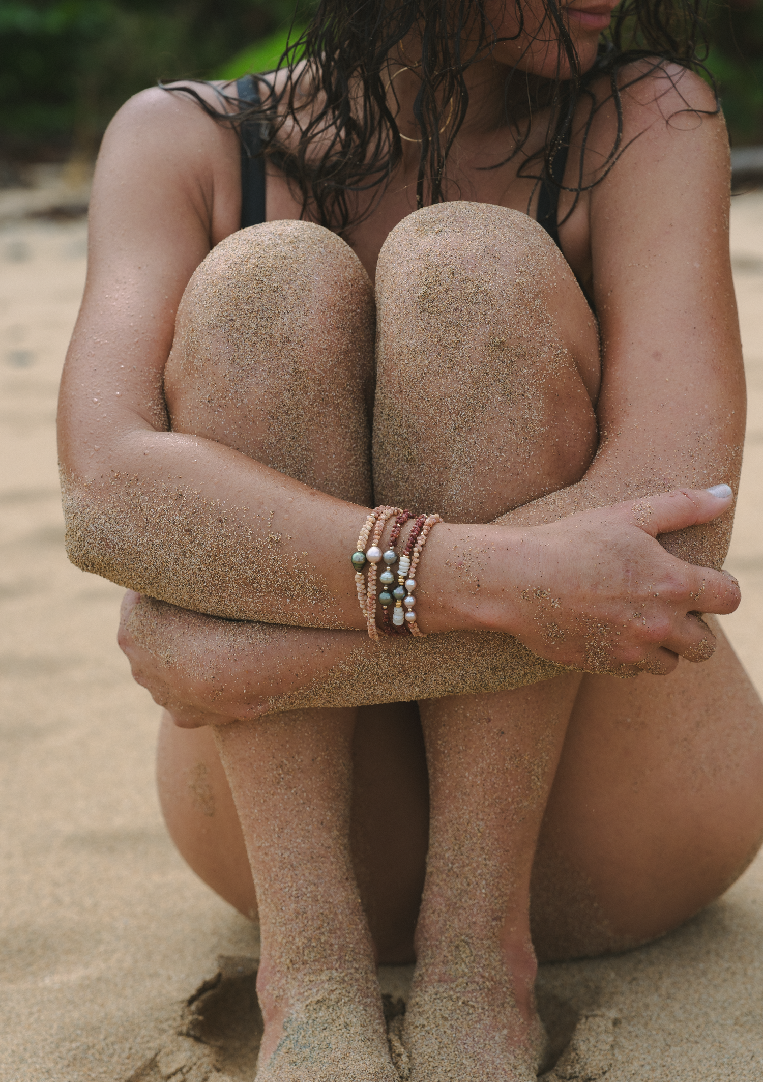 Sandy legs and feet curled up on a beach with bracelets.