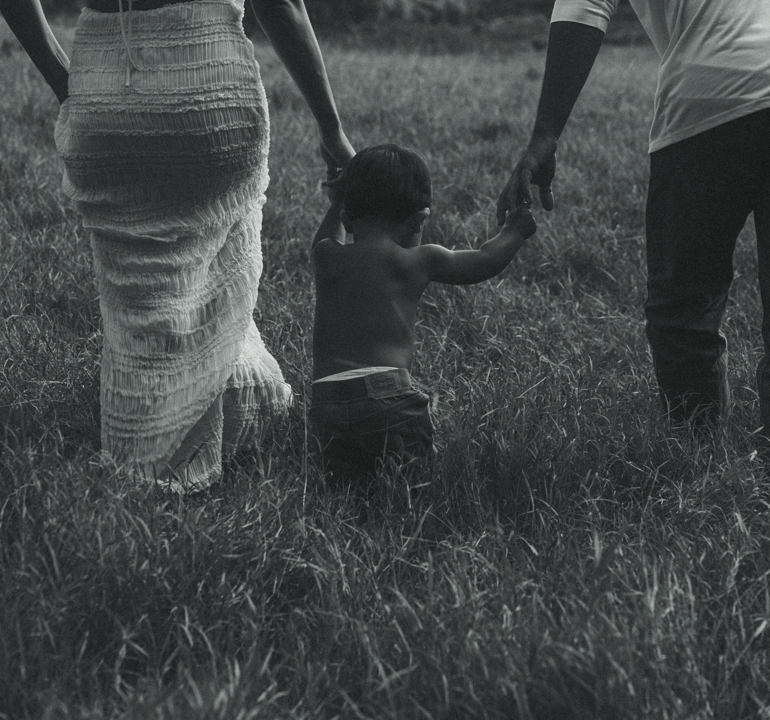 Black and white photograph showing people's legs and feet walking on grass in an outdoor setting.