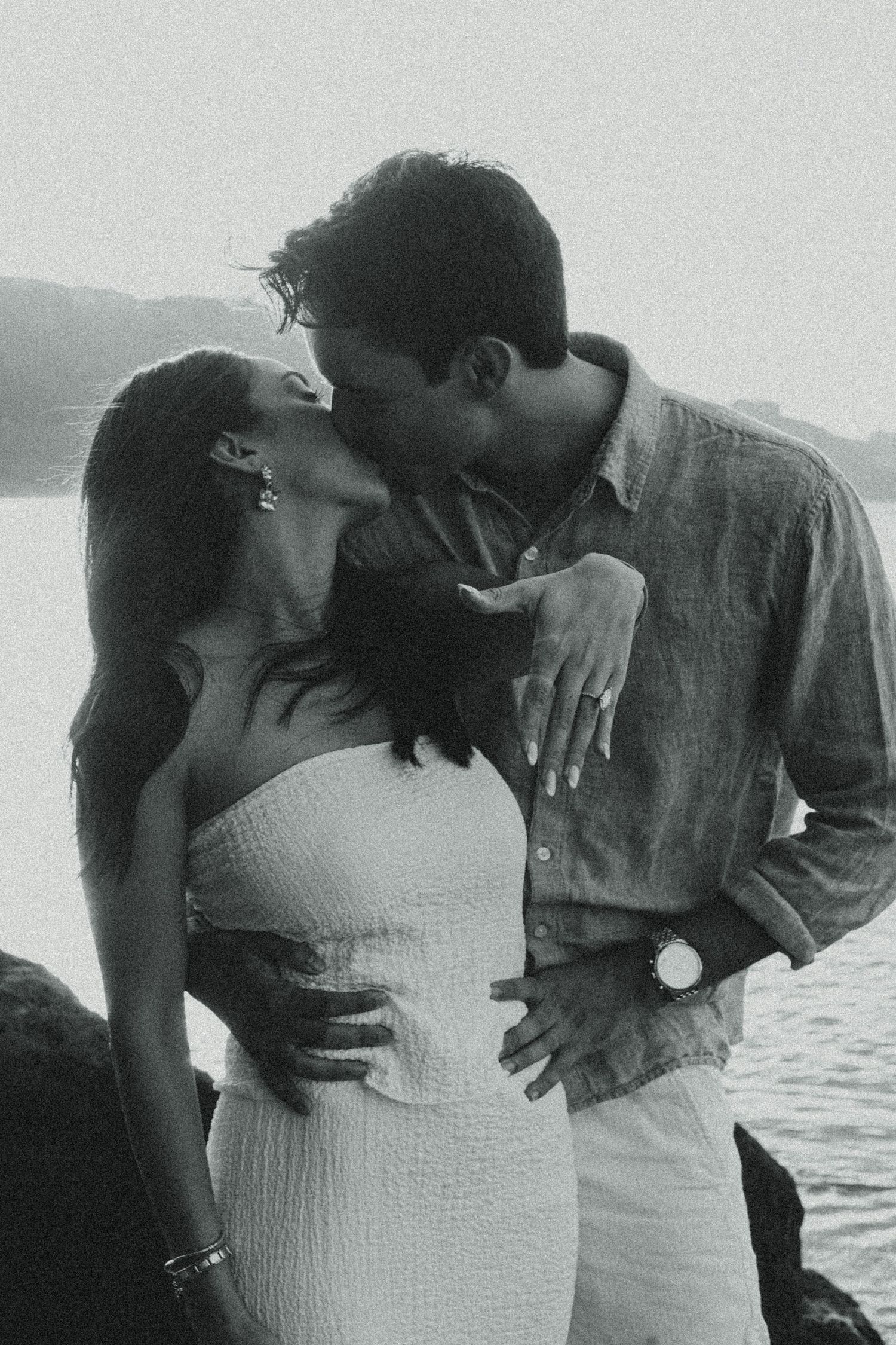 A romantic black and white photo of a couple sharing a tender kiss by the water.