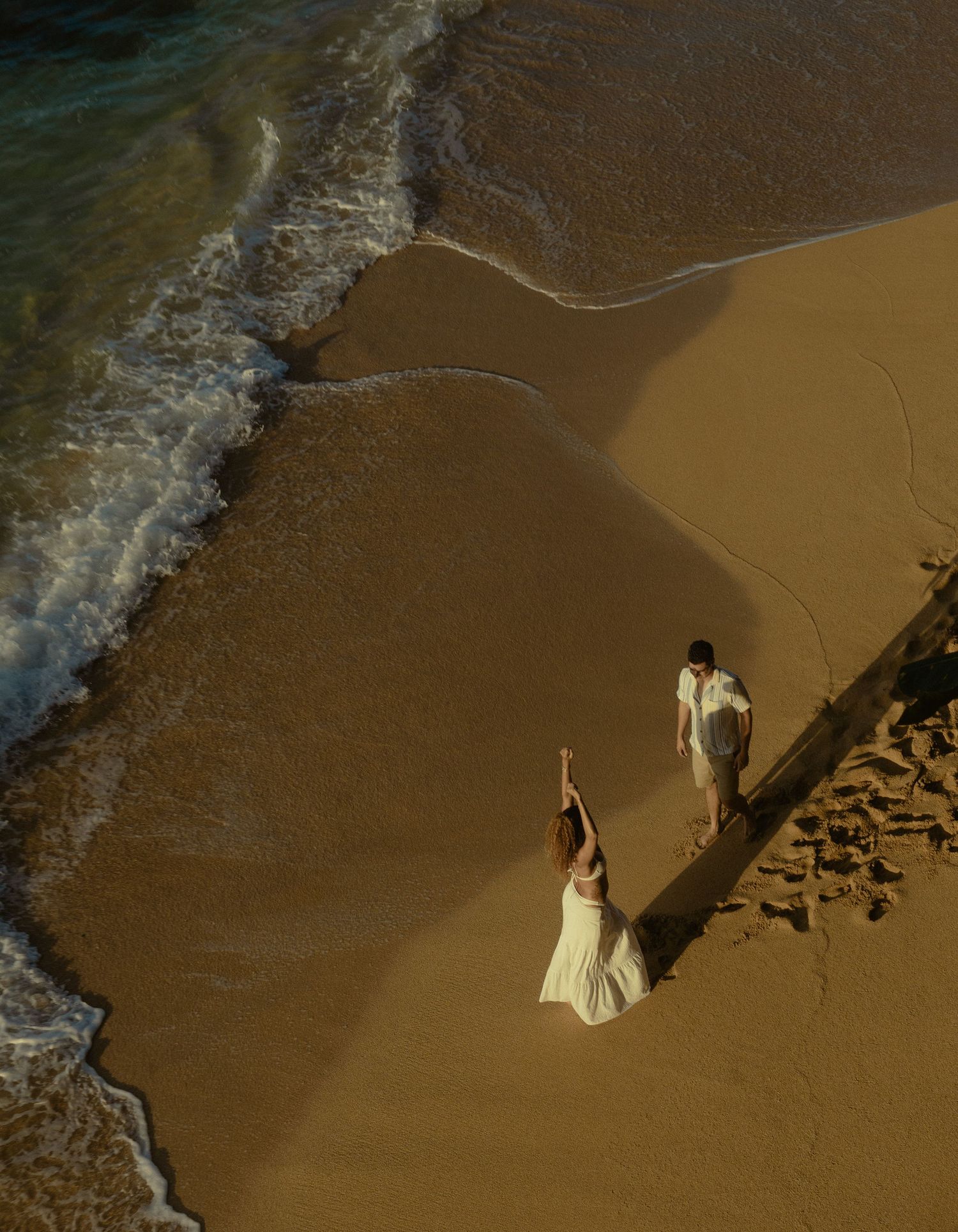 A sequence of aerial beach photos showing a person in white walking and making patterns in wet sand along the shoreline.