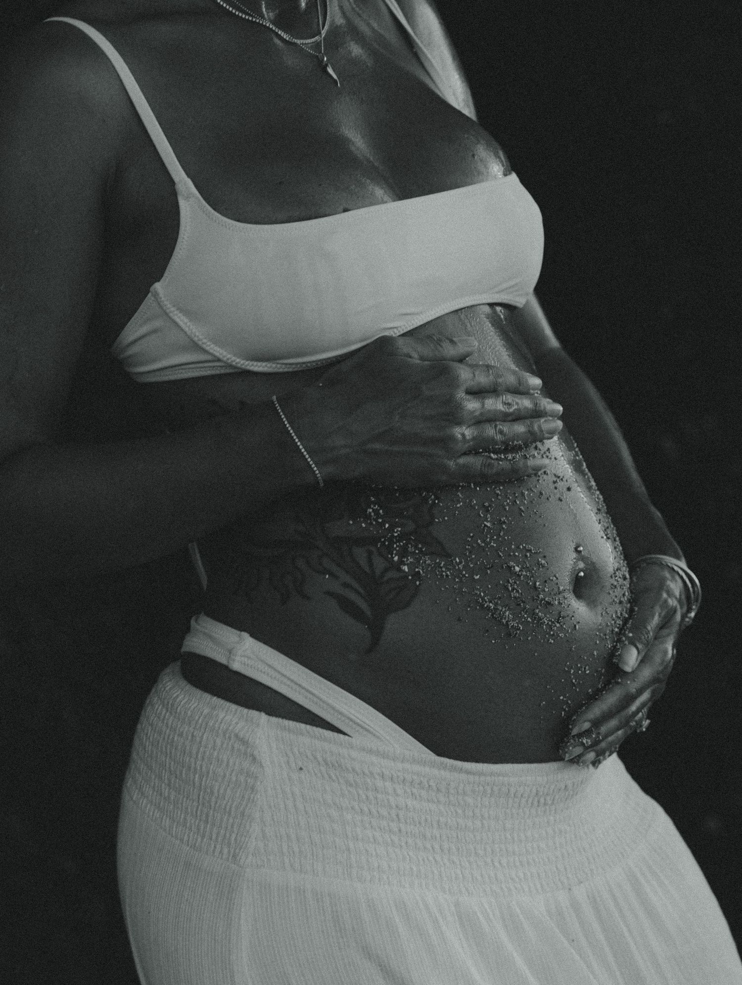 Black and white artistic maternity photos showing a pregnant belly with water droplets in dramatic lighting.