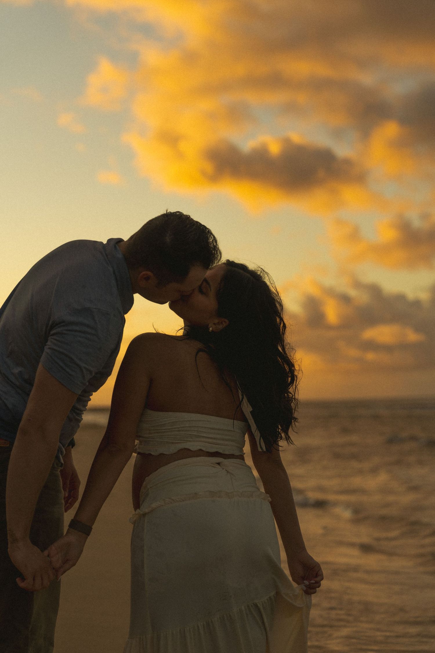 A romantic couple embraces on a beach during a dramatic golden sunset over the ocean.