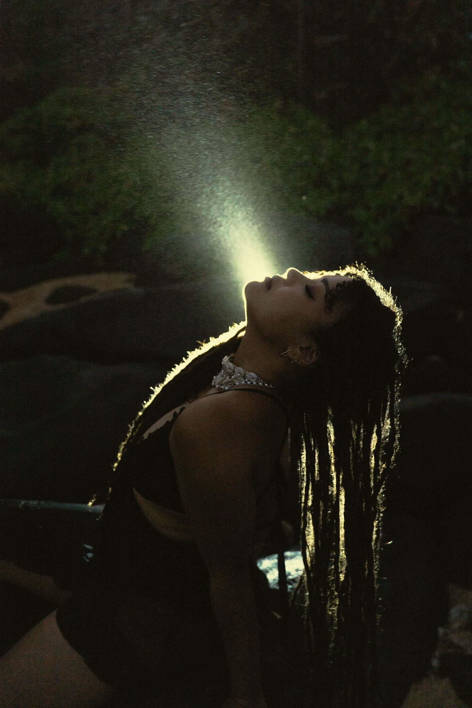 Silhouetted figure with braided hair illuminated by dramatic backlighting against a dark background.