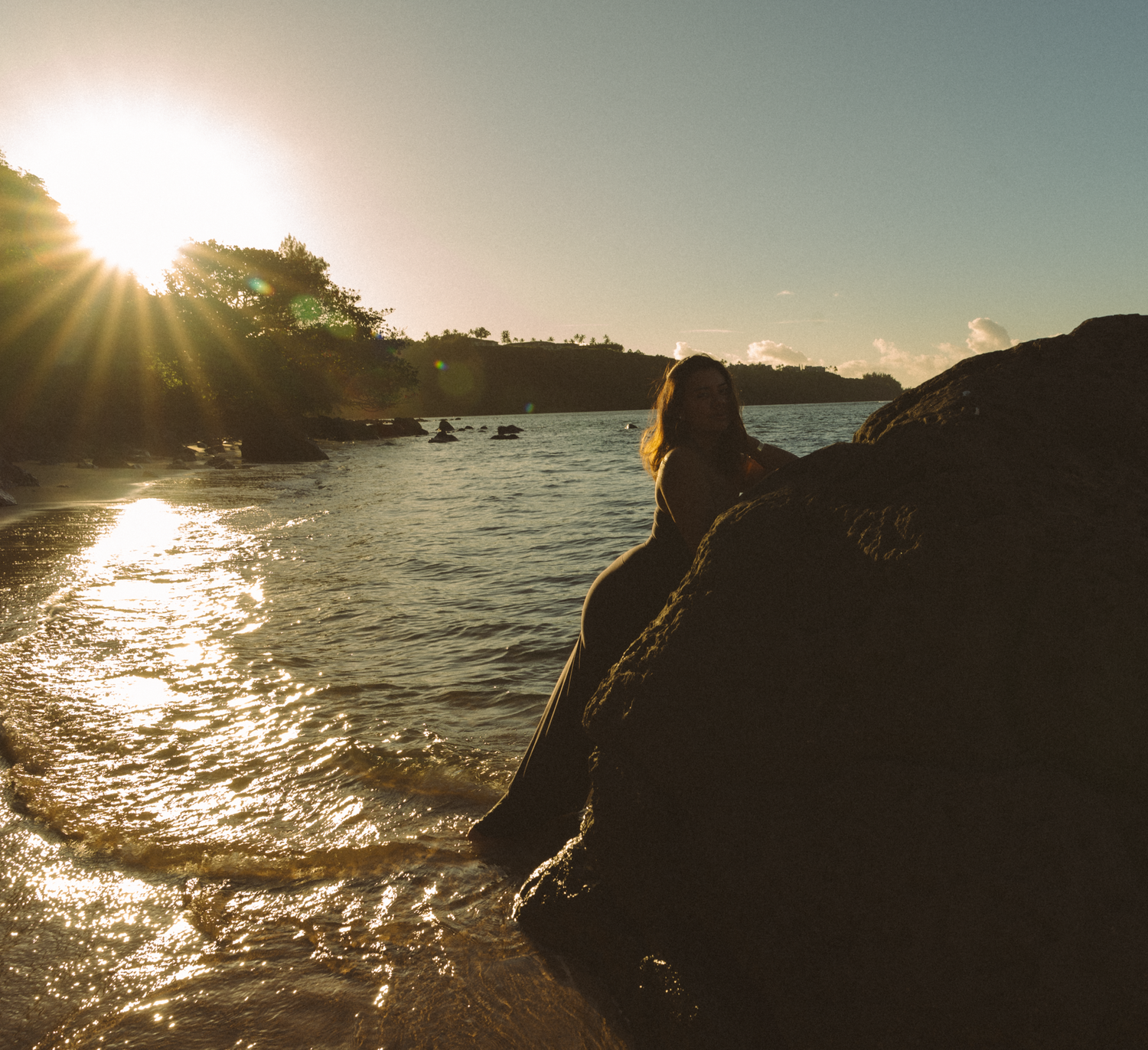 Golden sunlight sparkles on ocean waves against rocky coastal silhouette.