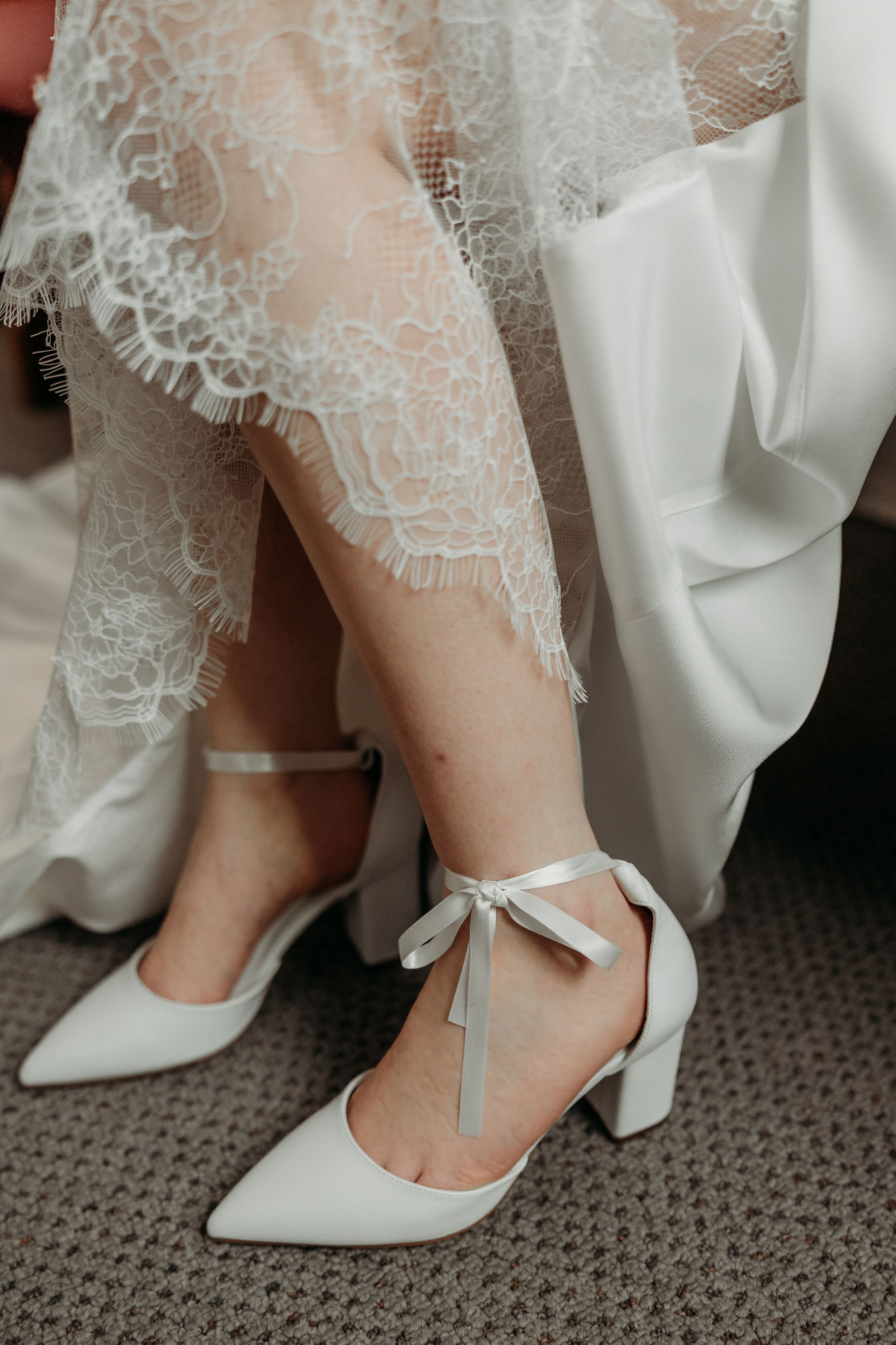 Detailed portrait of a bride's shoes and lacy wedding dress.