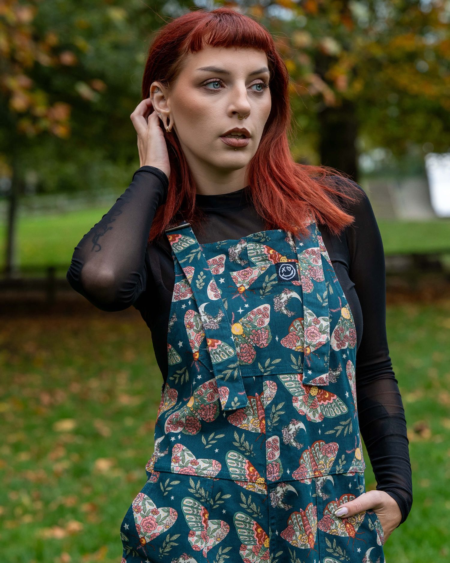 woman with double buns hairstyle wearing dark lipstick, a black lace-up top, and black shorts, standing with her hands i