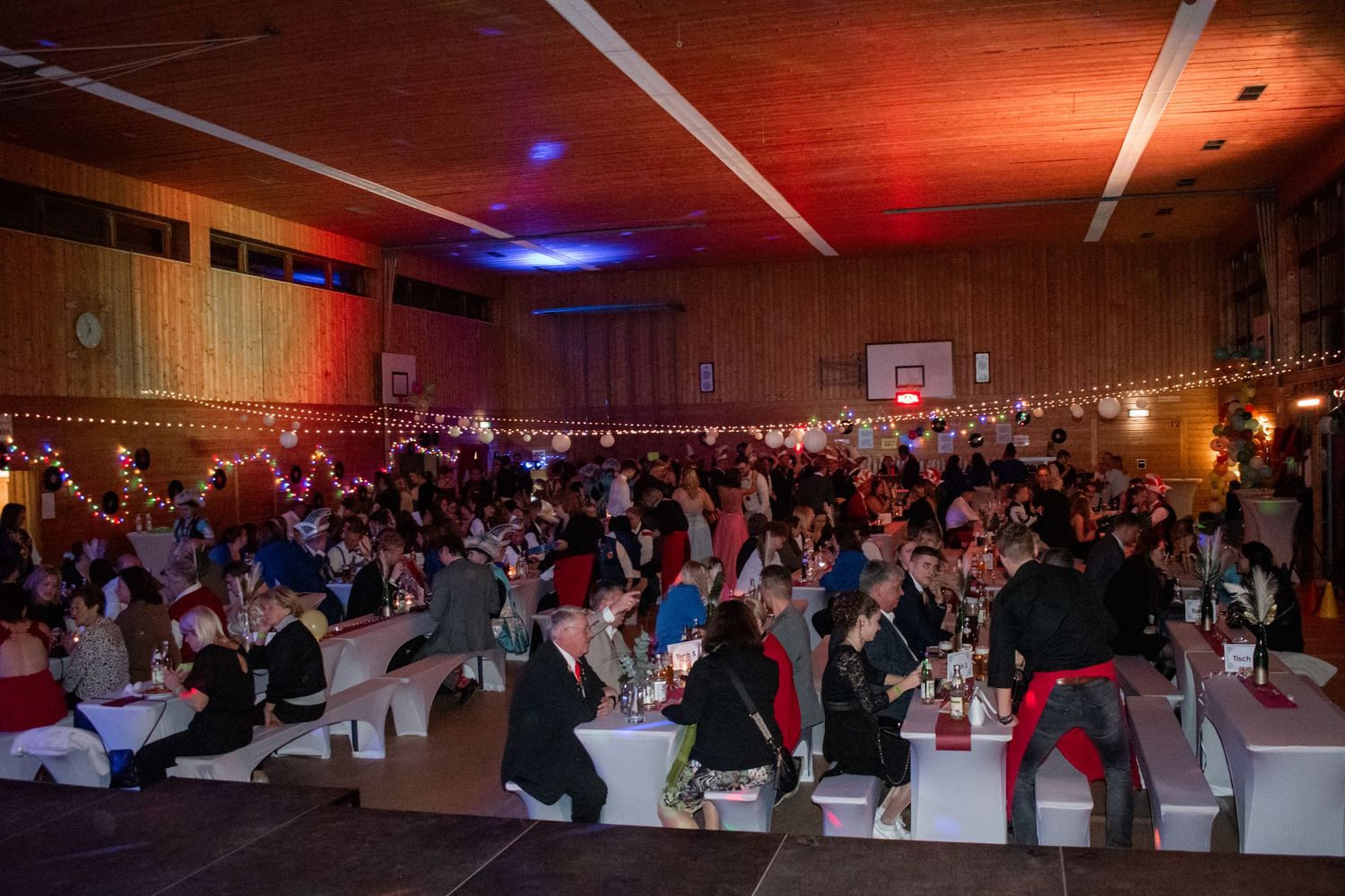 Large event hall with purple lighting and guests seated at round tables for a special occasion.