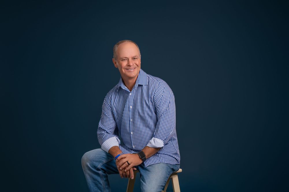 Professional headshot portrait of someone in a blue button-down shirt against a dark background.