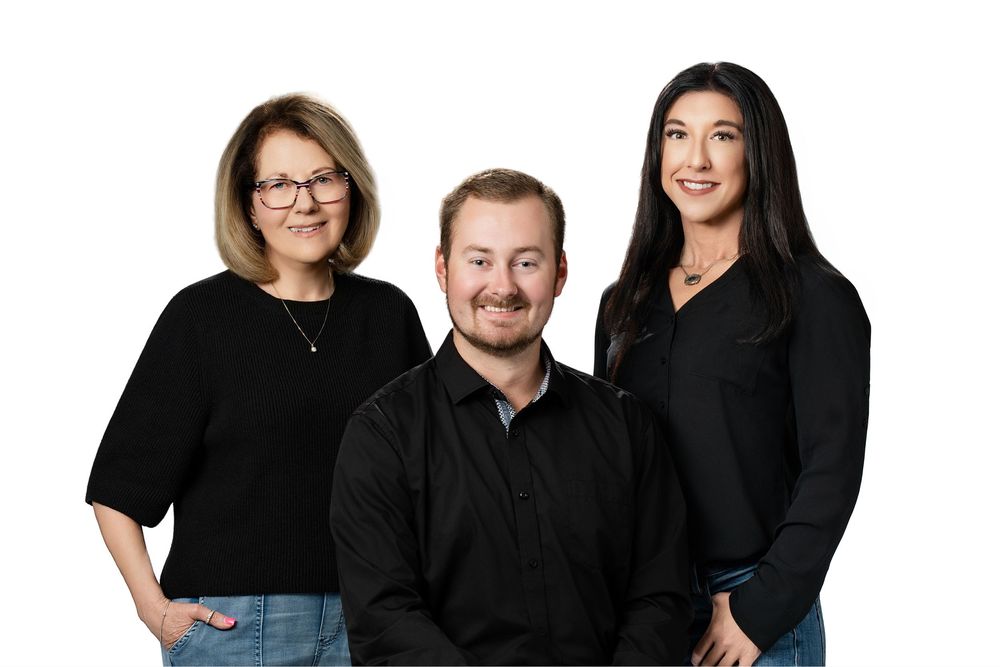 A group of people wearing black clothing pose together in a professional studio setting against a white background.