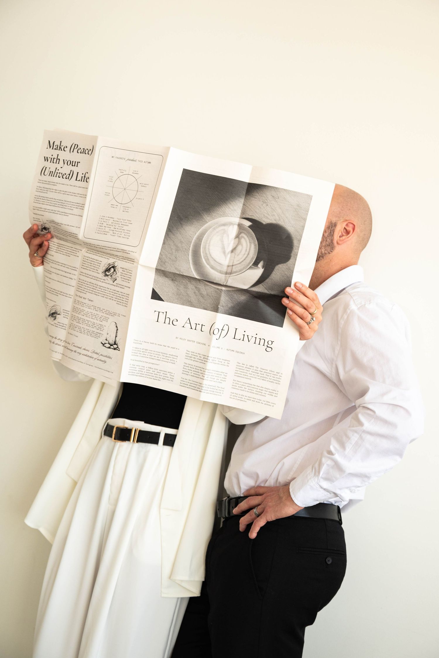 Two people relaxing on white bedding while holding up fashion photographs.