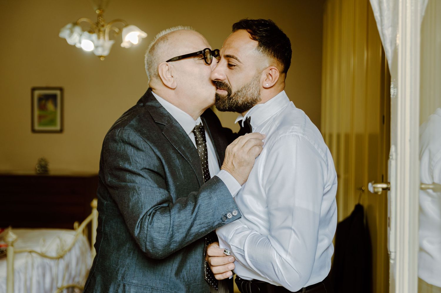 An intimate embrace between two people in formal attire against a warm interior setting.