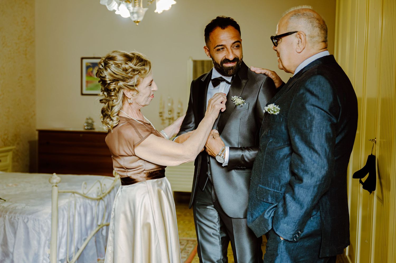 Three people in formal attire share a joyful moment during a wedding celebration.