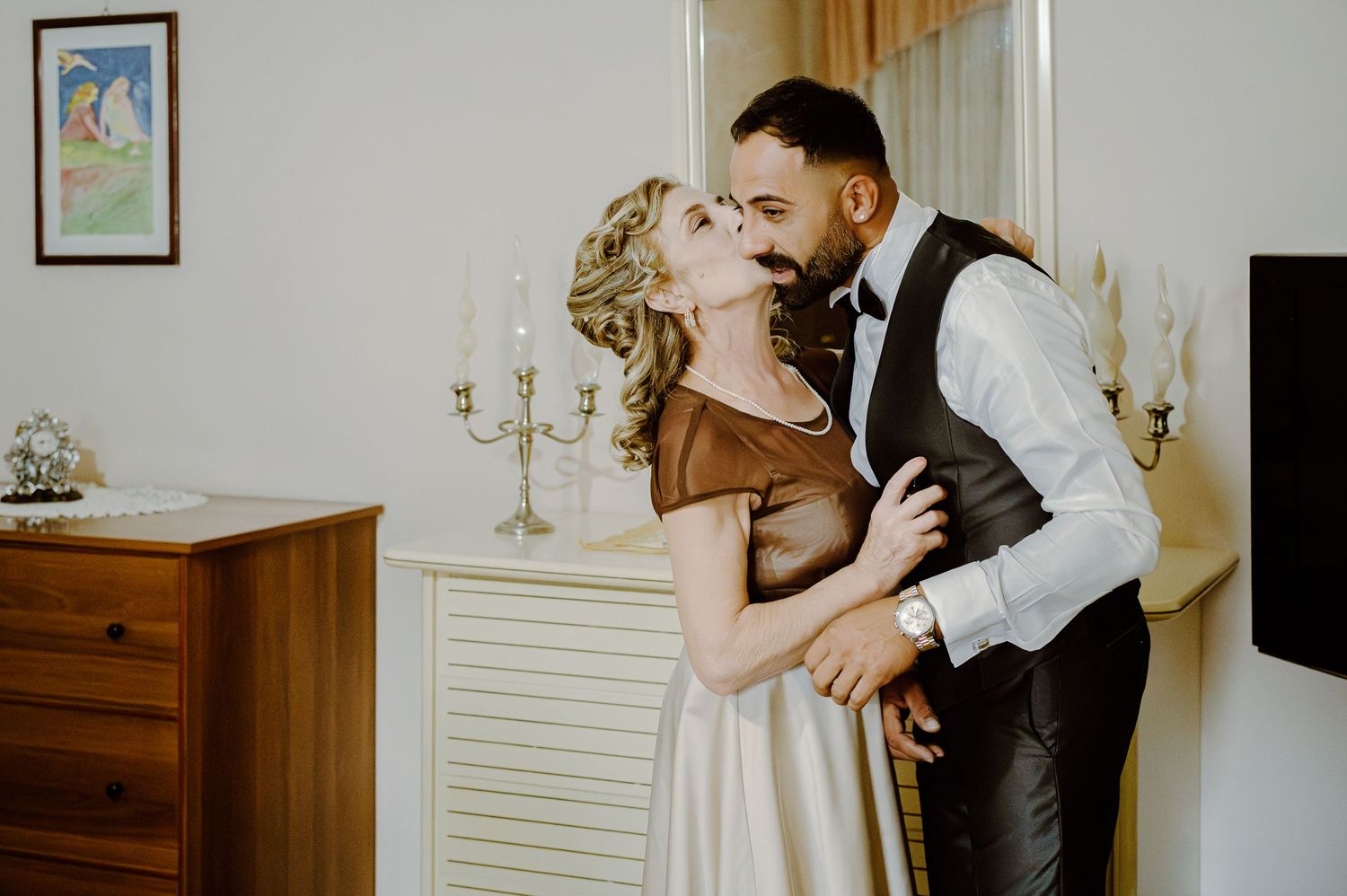 A romantic moment between a couple in formal attire near vintage furniture and candelabras.