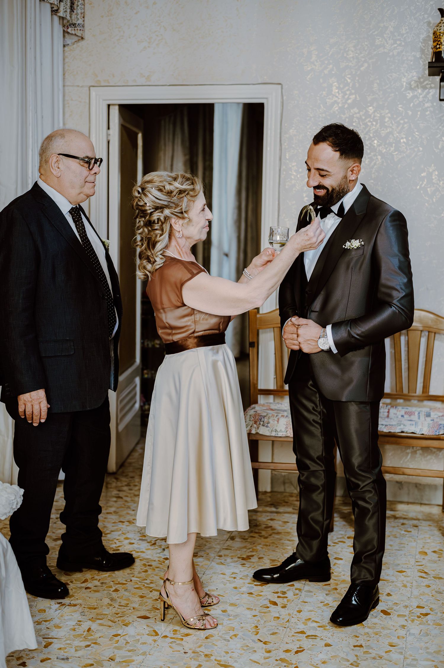 Three people in formal attire share a candid moment in an elegantly decorated room.